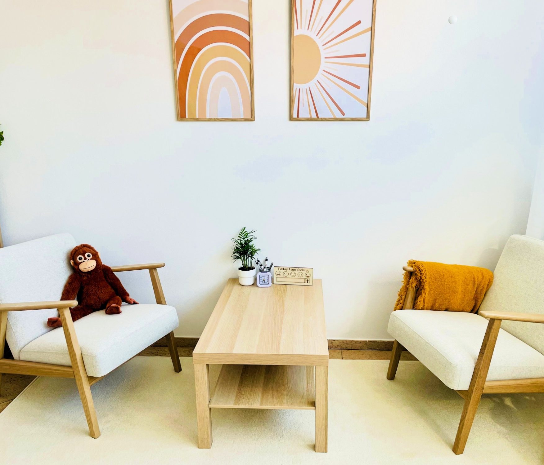 Zwei Sessel mit einem Tisch, dekoriert mit Pflanzen und Bildern an der Wand. Ein Plüschaffe sitzt.